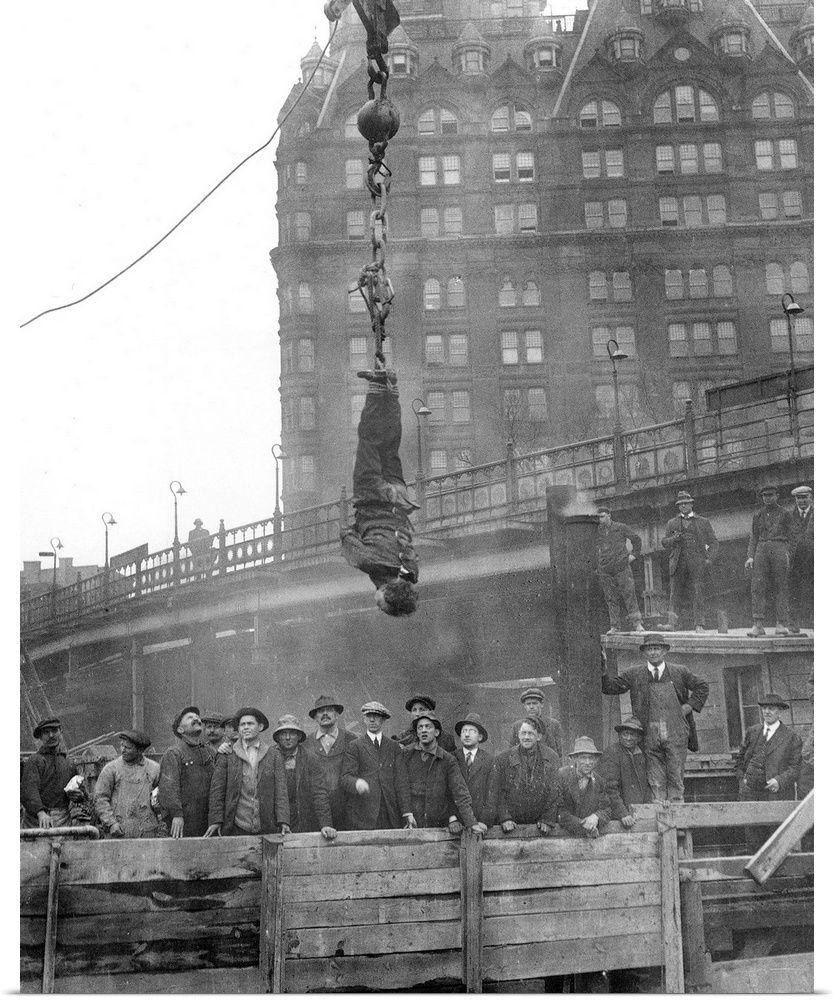 American magician. Houdini in a straitjacket suspended in midair over a subway excavation in New York City; photographed i...