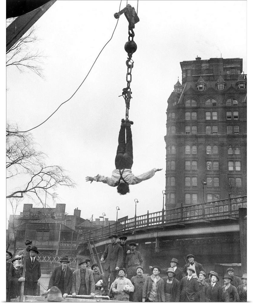 American magician. Houdini at finish of stunt of releasing himself from a straitjacket while suspended in midair; photogra...