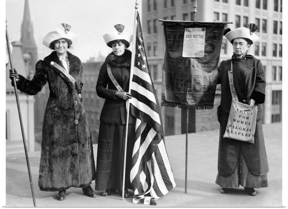 Three women photographed on a Brooklyn rooftop before a demonstration for women's right to vote. One woman holds a poster ...