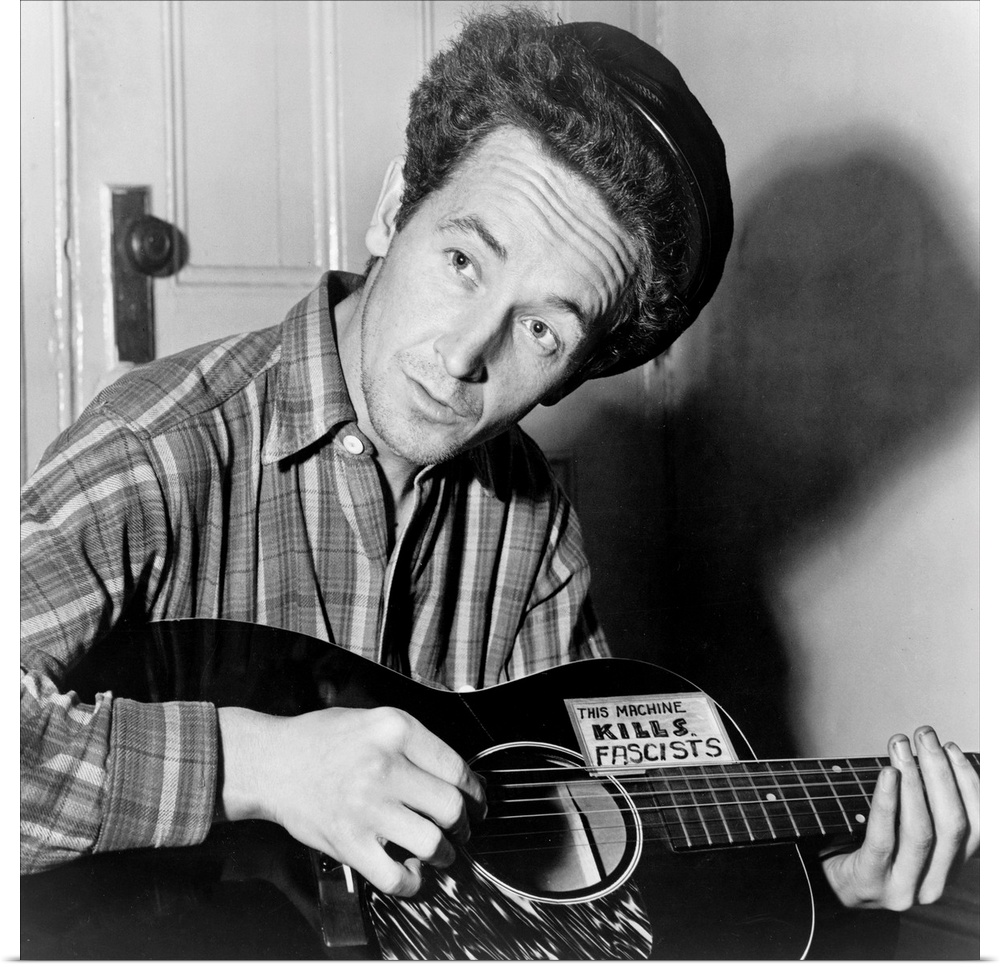 American folk singer. Photographed playing a guitar that has a sticker attached reading: 'This Machine Kills Fascists.' Ph...