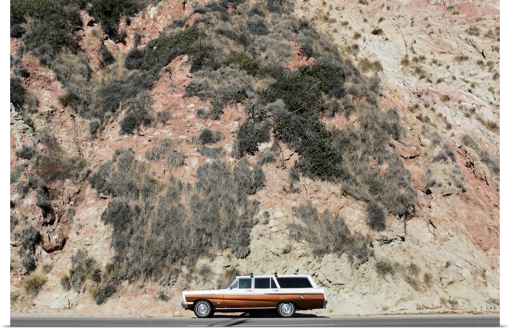Photograph of a vintage station wagon sitting on the side of a road next to a rocky hill.