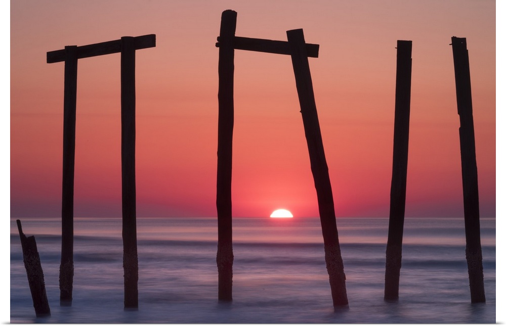 Old pilings from a fishing pier framing a sunrise on the ocean horizon, Ocean City, New Jersey.
