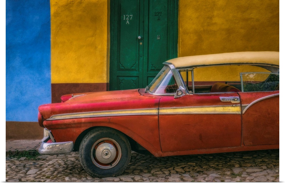 A bright red vintage car parked against a yellow and blue wall with a green door in the streets of Havana, Cuba.