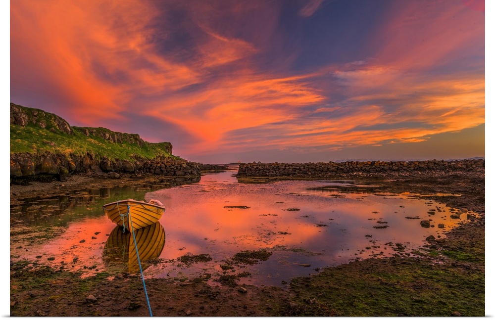 A canoe moored at low tide under vivid sunset clouds in Iceland.