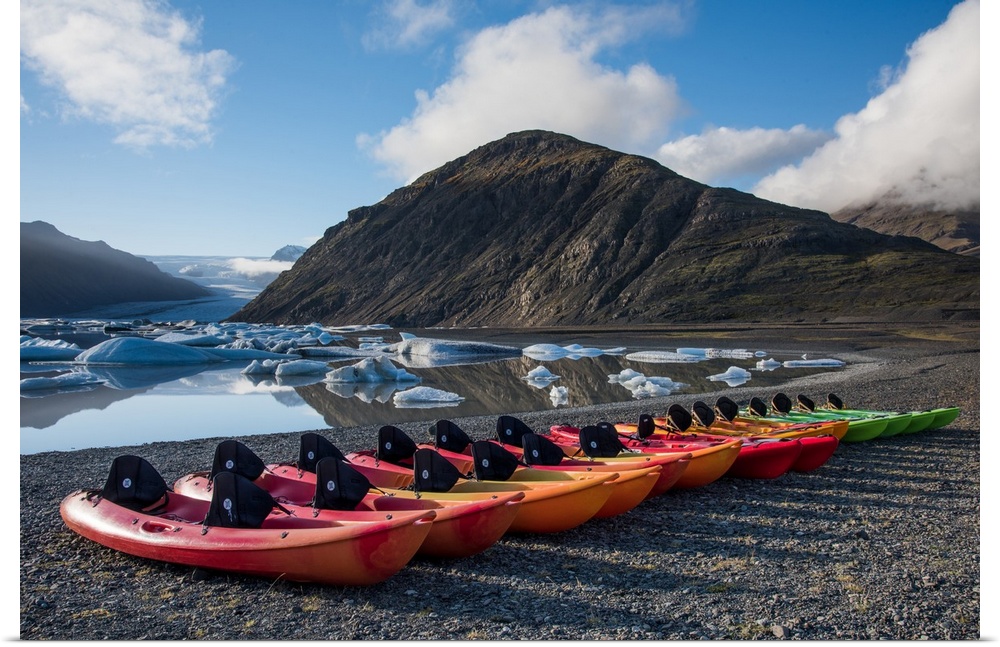 A row of kayaks lined on the shore by an icy lake in Iceland.