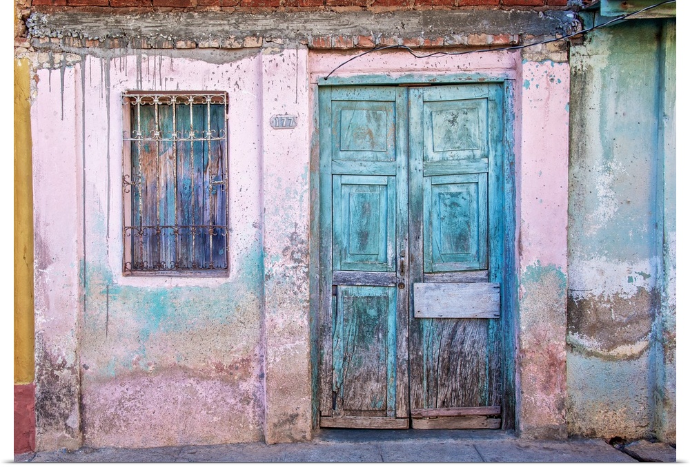 Weathered front of a building with pink paint and blue doors in Havana, Cuba.