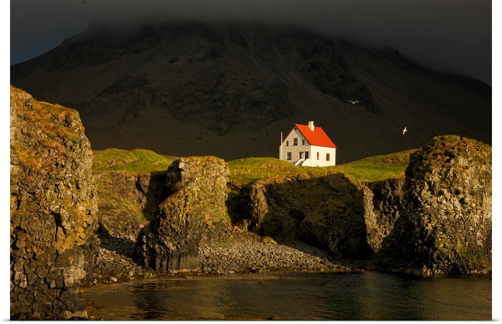 A small white house with a red roof on the steep cliffside of Snaeflesnes, Iceland.