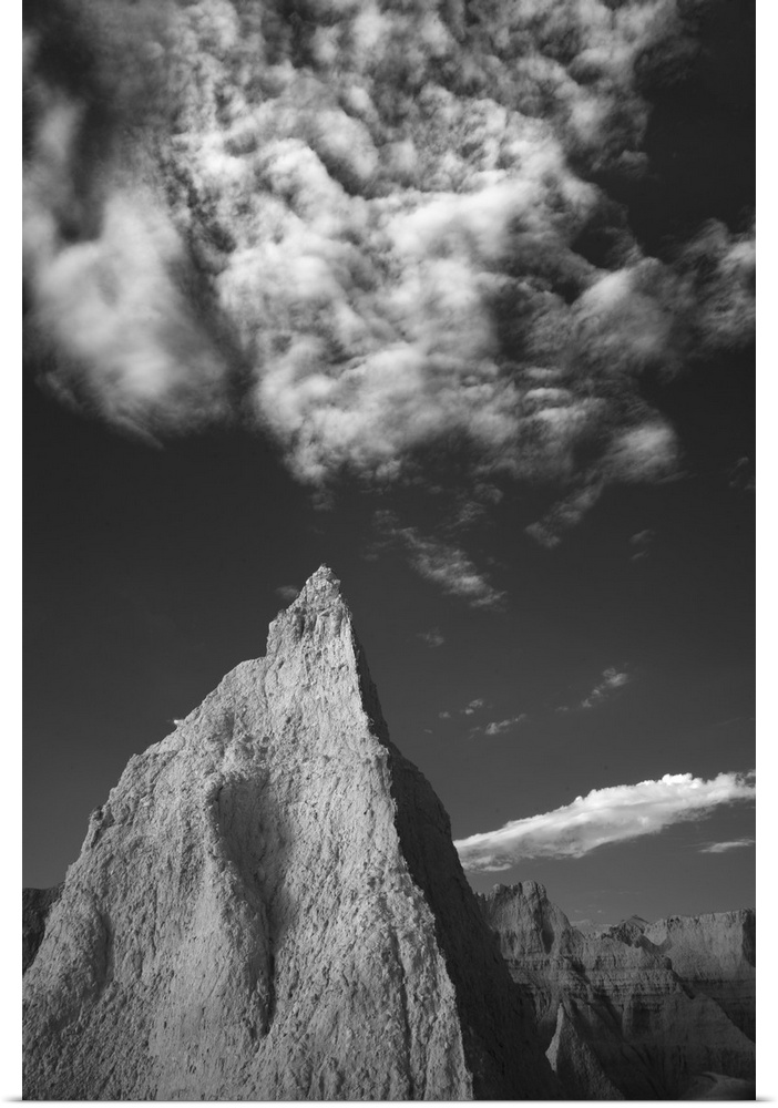 Black and white photo of a tall rock formation pointing towards clouds in the sky in the Badlands, South Dakota.