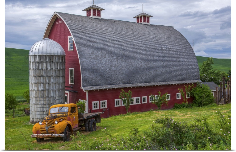 A large red barn and an orange truck against the green landscape of Palouse, Washington.