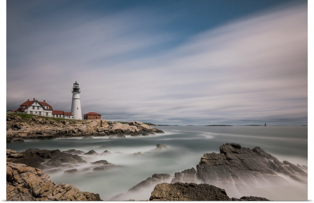 Lighthouse on the rocky coast of Maine with sweeping clouds above.