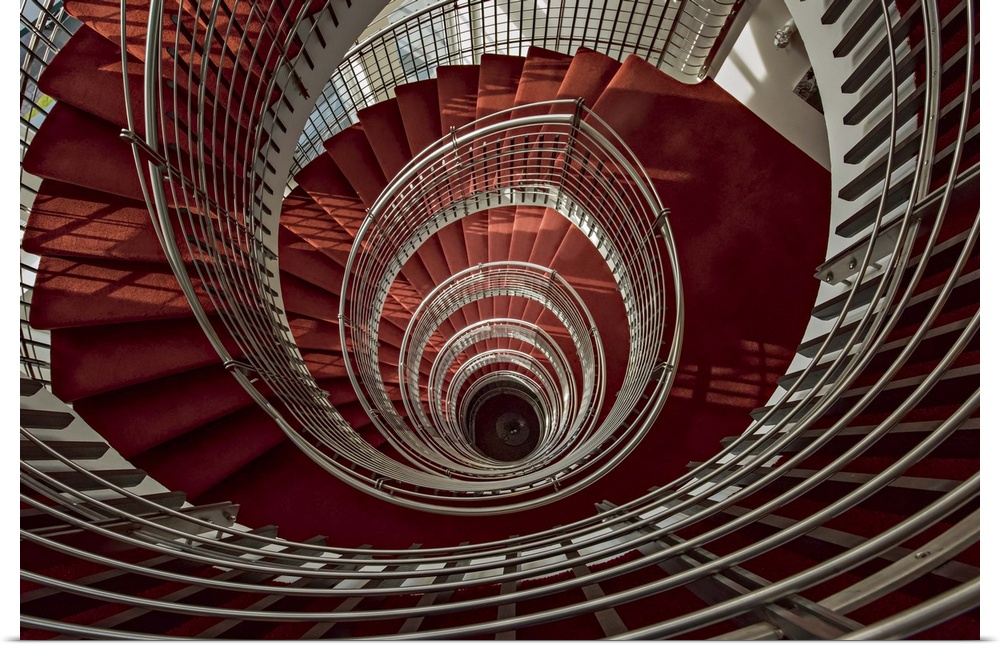 View through the center of a spiral staircase with red steps and white railings.