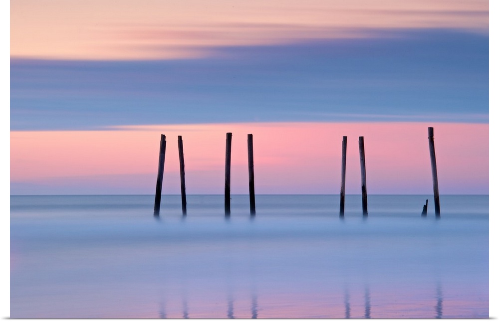 Silhouettes of seven pilings in the ocean at sunset in New Jersey.