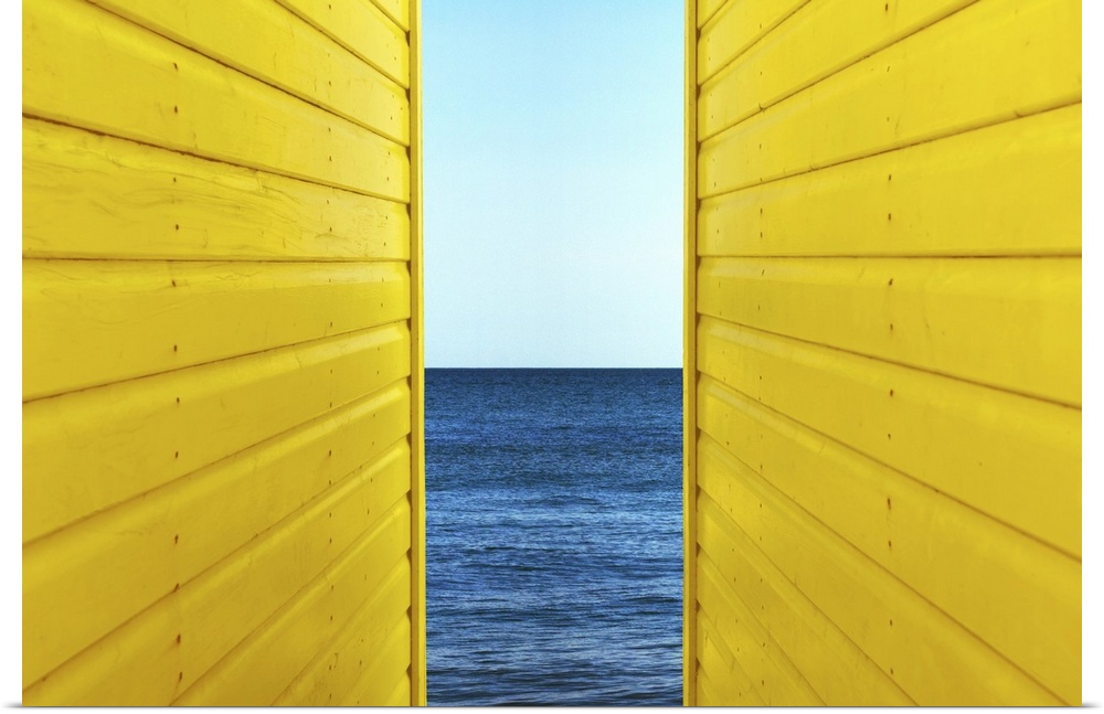 Symetrical perspective of 2 Yellow Beach Huts with blue sky and sea inbetween them.