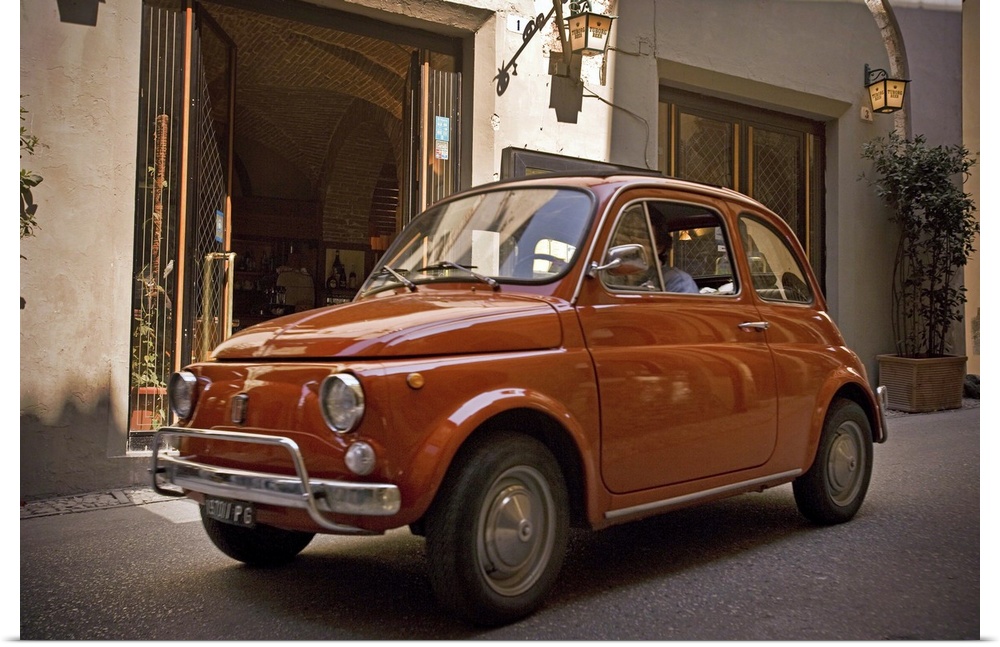 A small red car drives through the narrow streets in the downtown area of an Italian city.