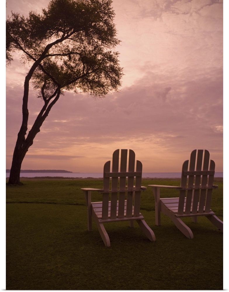 Adirondack chairs sit on a grassy field at sunset.