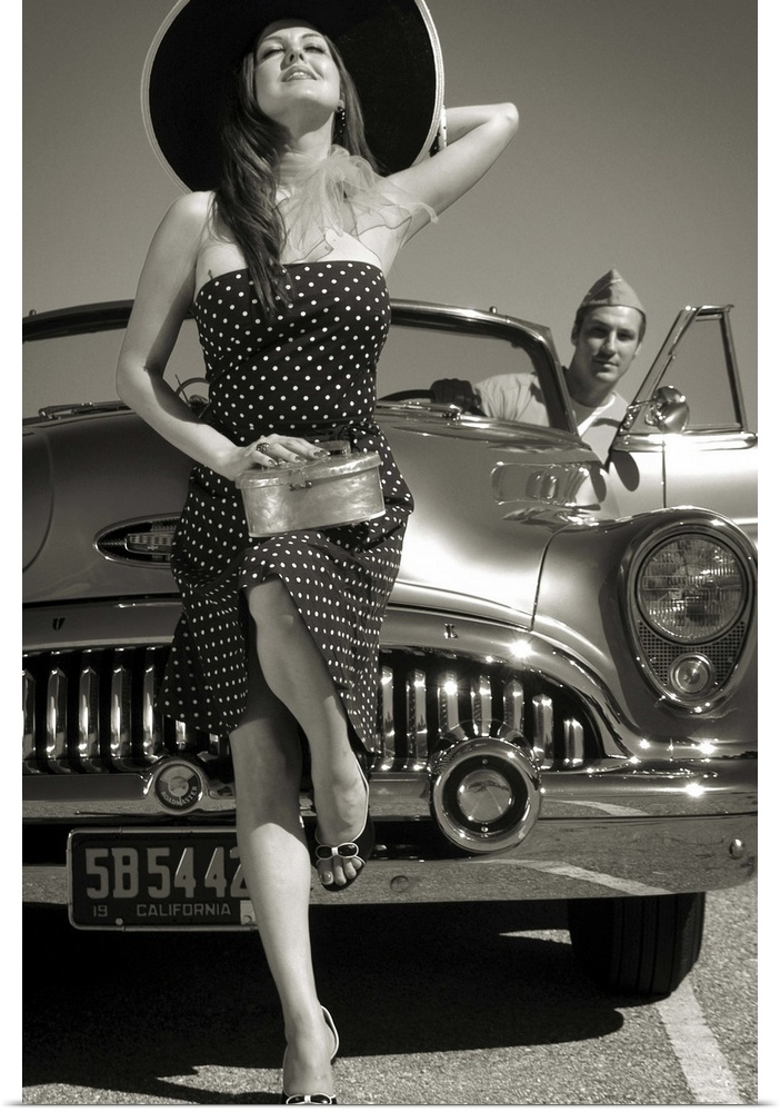 A model wearing a large hat and a spotted dress with a 50's car