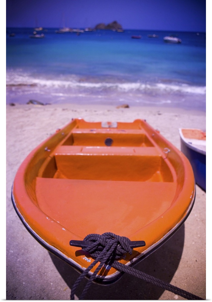An colorful orange row boat on a Caribbean beach in front of the turqoise Caribbean Sea.