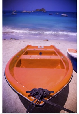 An colorful orange row boat on a Caribbean beach in front of the turqoise Caribbean Sea