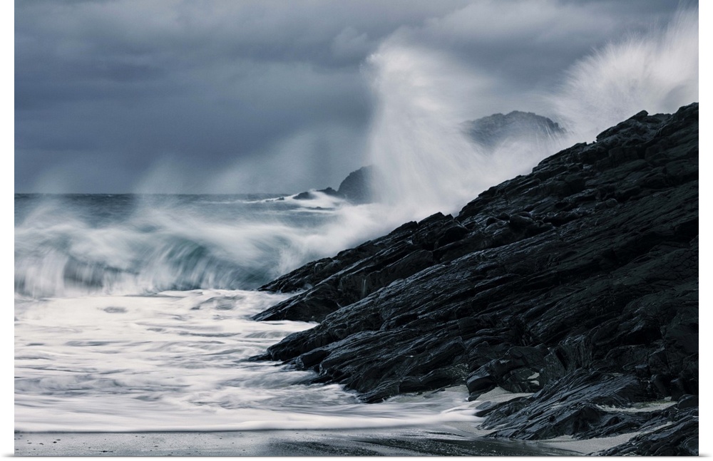 Crashing waves on a stormy Scottish beach with dark rocks under grey sky