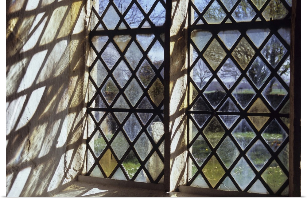 Detail of stone-framed church window with diamond-leaded panes of clear or pale yellow glass throwing interesting shadows