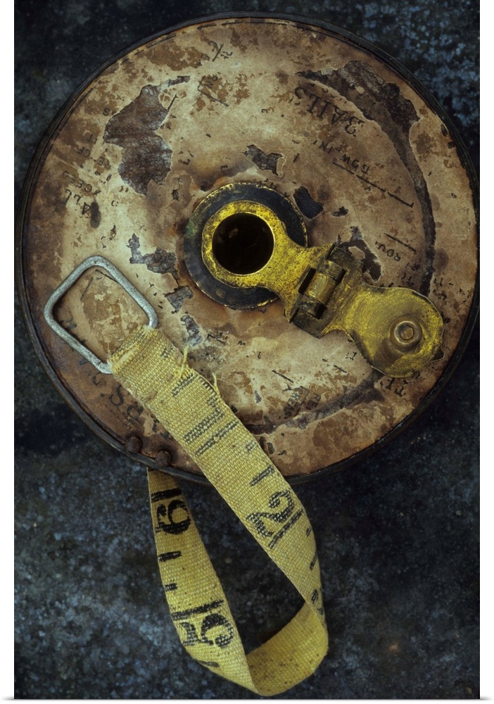 Groundsmans measuring tape in well worn metal case with brass winding handle lying on tarnished metal sheet