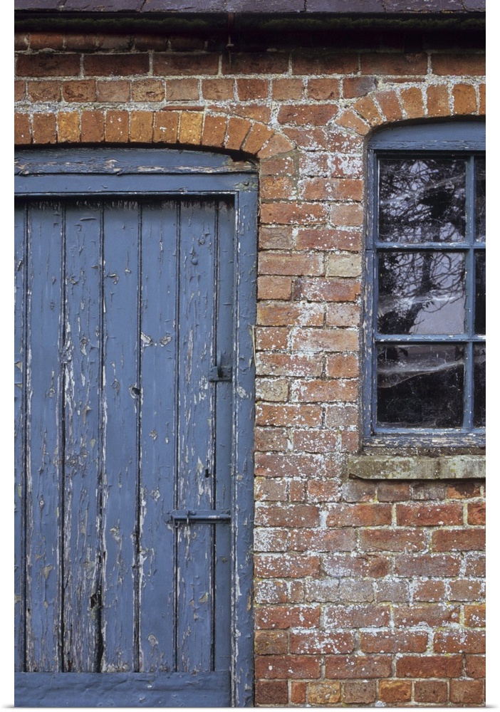 Detail of old orange brick stable block or barn with flaking blue painted wooden door and windows and slate roof