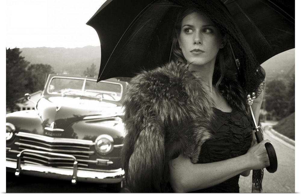 A model holding an umbrella standing near an old car