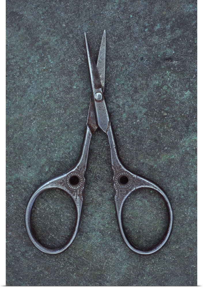 Antique steel sewing scissors decorated with small pattern lying on tarnished metal