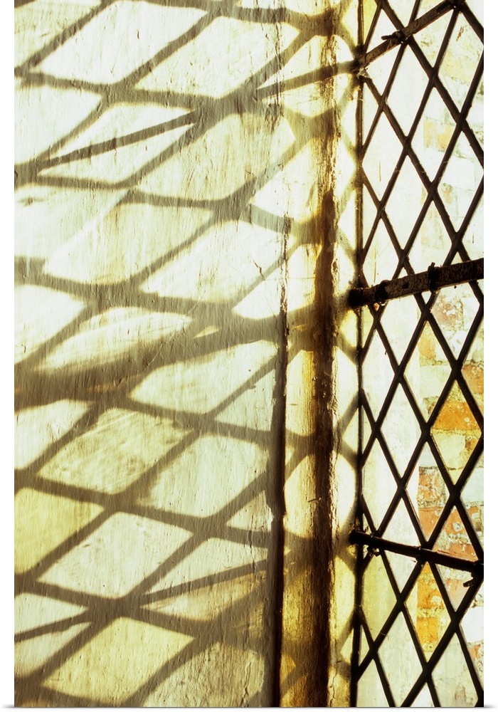 Detail of stone-framed window with diamond-leaded panes of clear or pale yellow glass throwing shadows onto niche wall
