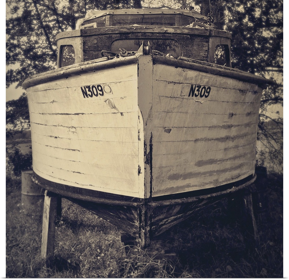 Bow view of an old holiday cruiser moored on dry land under trees