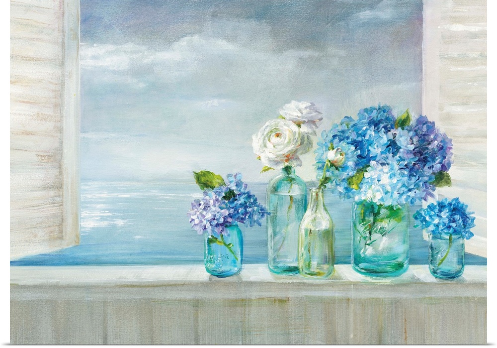 A collection of flowers in blue glass vases on a windowsill overlooking the ocean.