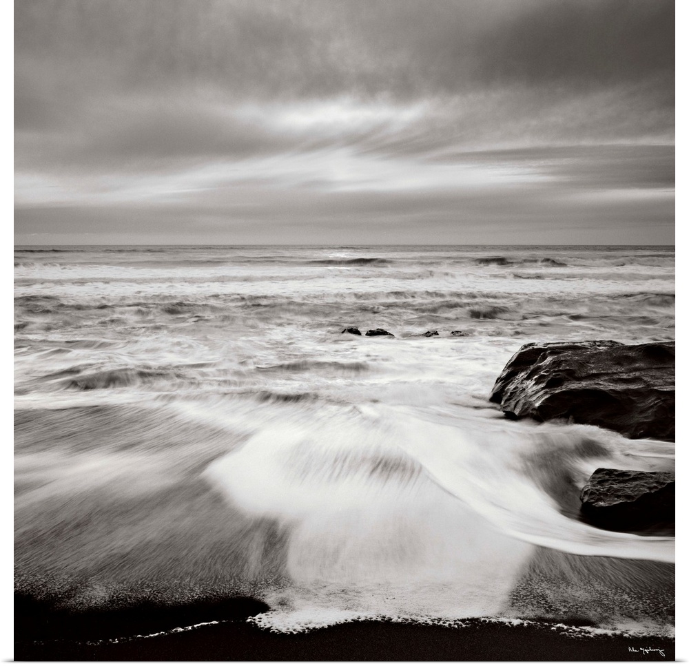 Black and white photograph of a seascape with the ocean waves hitting the rocky shoreline.
