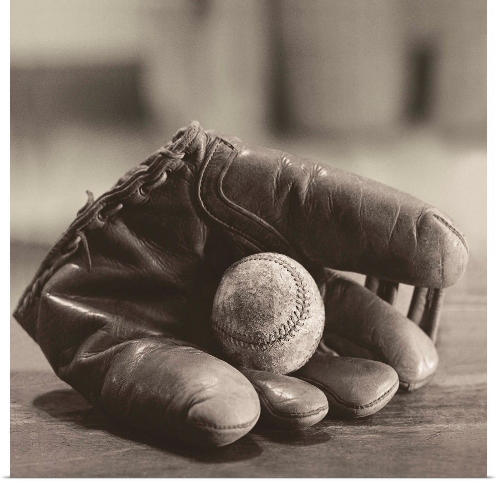 Square sepia toned photograph of a worn baseball in a vintage mitt on a soft focus backdrop.