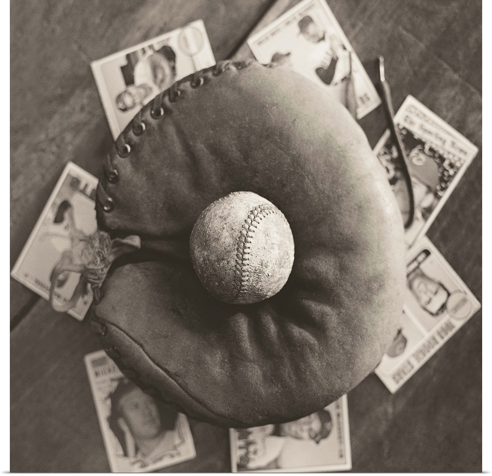 Square sepia toned photograph of a worn baseball in an old mitt and vintage baseball cards behind it.