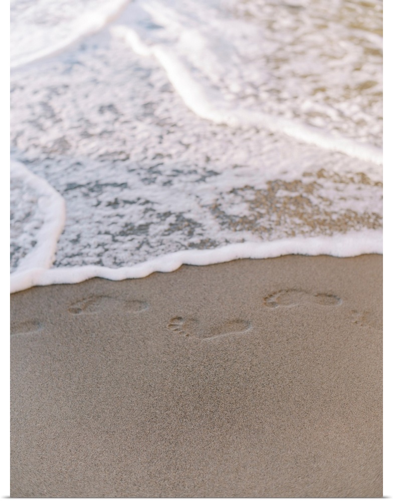 A photograph of small footprints in the sand about to be lapped with gentle waves.