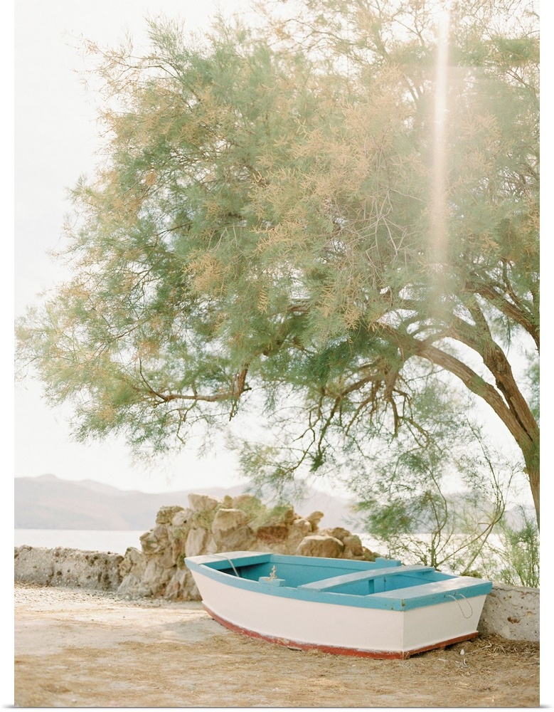 Photograph of a small wooden boat underneath a tree next to the water, Milos, Greece.