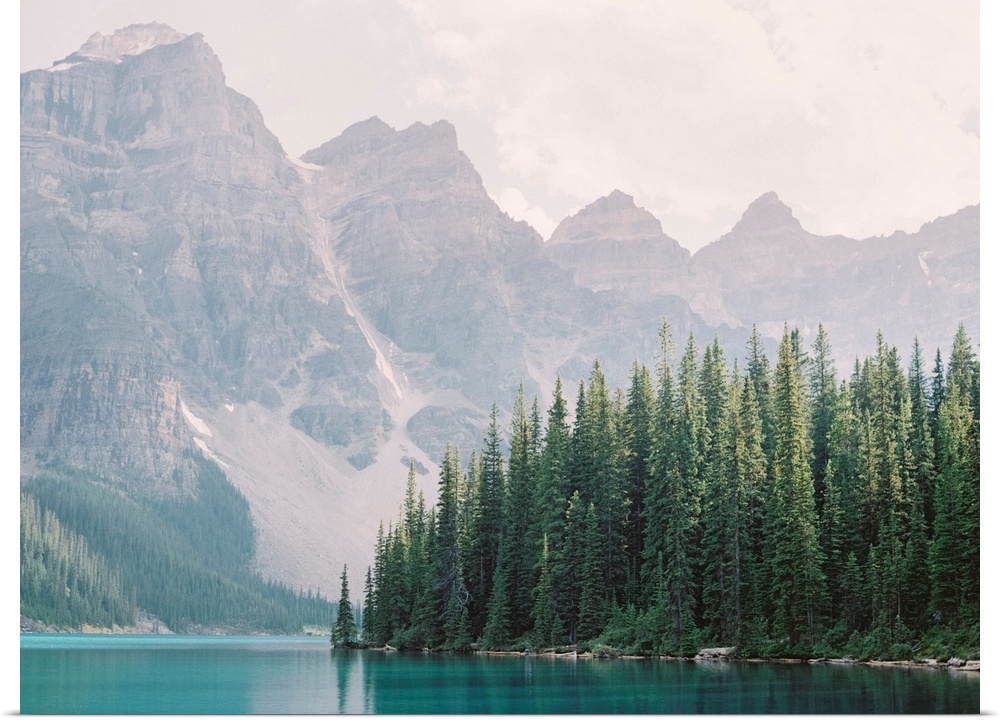 Photograph of tall evergreen trees at the edge of a clear blue lake, Moraine Lake, Banff national park, Canada.