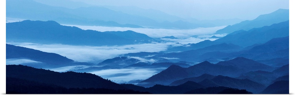 Panoramic landscape photograph of blue mountains covered in fog.