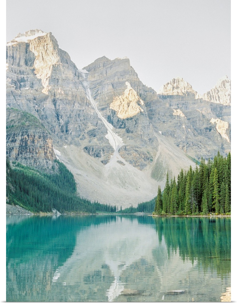 A vertical photograph of the mountains and trees reflected in Moraine Lake, Banff national park, Canada.