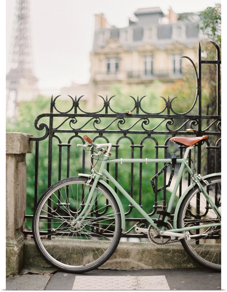 Photograph of a bicycle leaning against an ornate metal railing with the Eiffel tower in the distance.