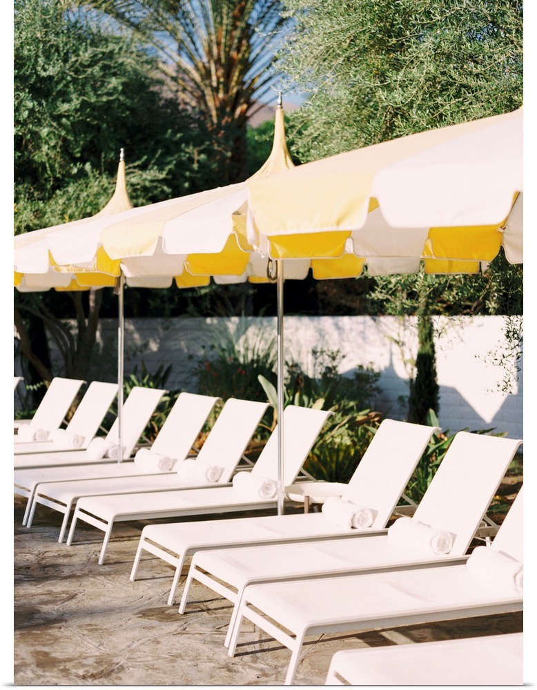 Photograph of a neat row of pool loungers with rolled towels underneath yellow umbrellas.