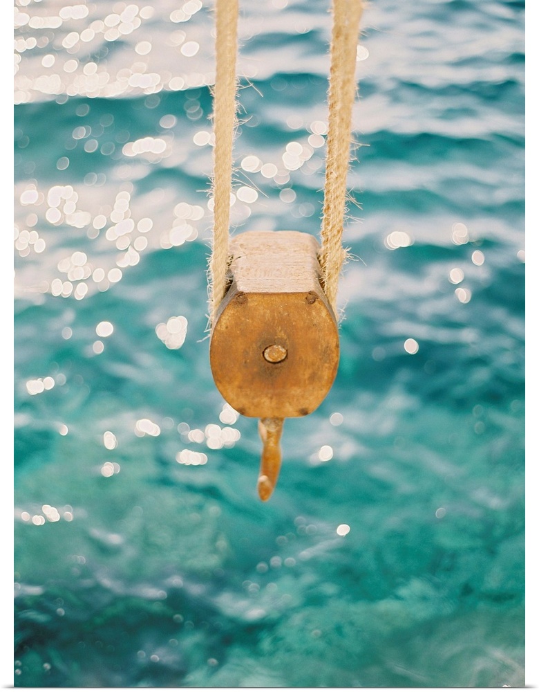 Photograph of a tackle block hanging over the clear blue water, Santorini, Greece.