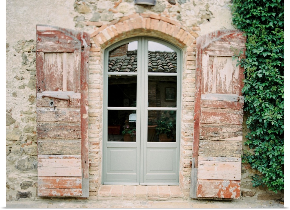 Photograph of pale grey-green double doors flanked by antiqued wooden shutters, Tuscany, Italy.