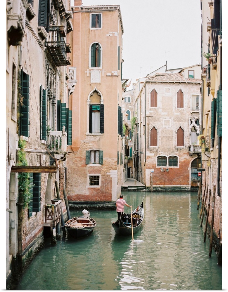 Photograph of a gondolier steering his way through the canals of Venice, Italy.