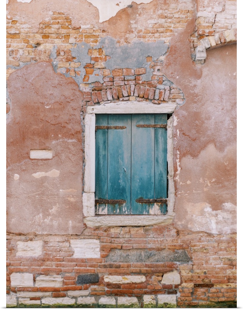 An architectural photograph of a set of small blue shutters set in a rustic brick and stucco wall in Venice, Italy.