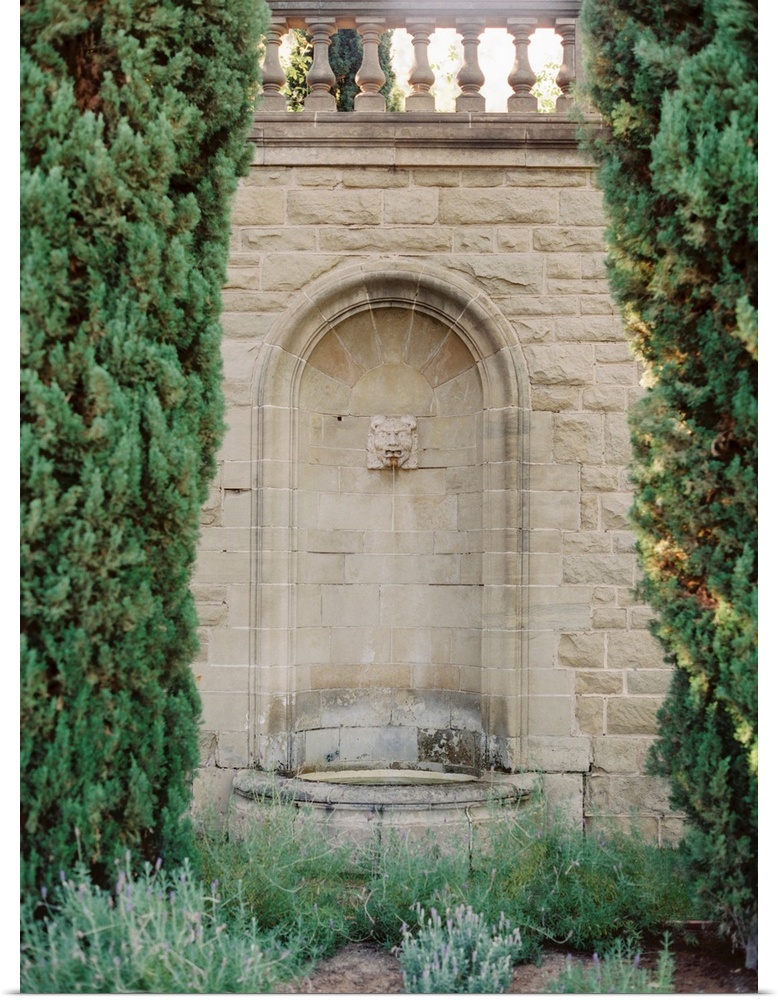 A photograph of an ornate fountain set into the wall amidst elegant gardens of a Mediterranean villa.