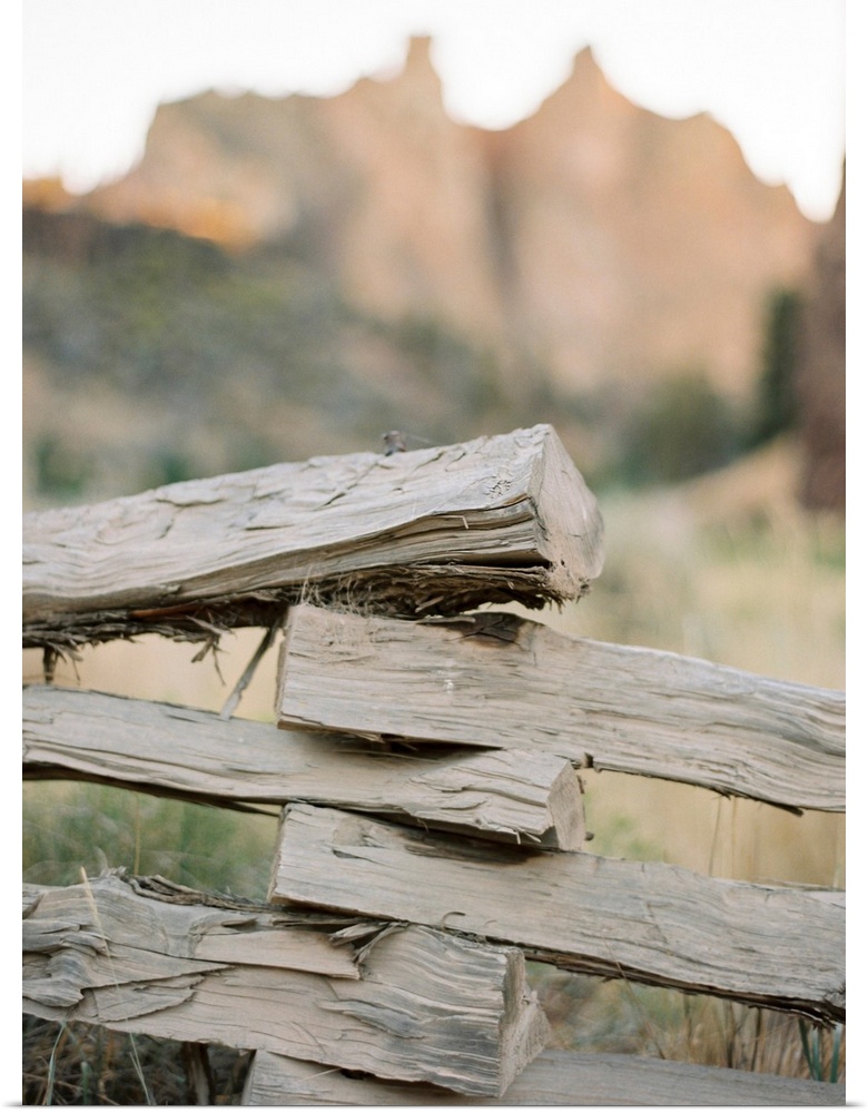 A close up photograph of a rustic split rail fence in front of a large mountain.