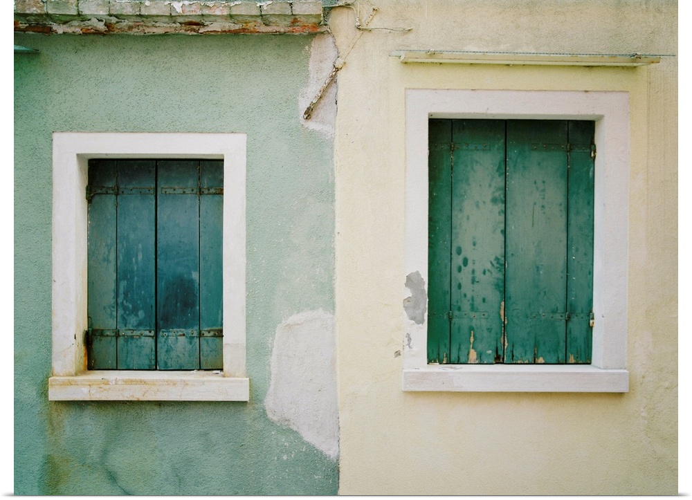 Photograph of a blue house next to a white house, both with old wooden shutters, Burano, Italy.