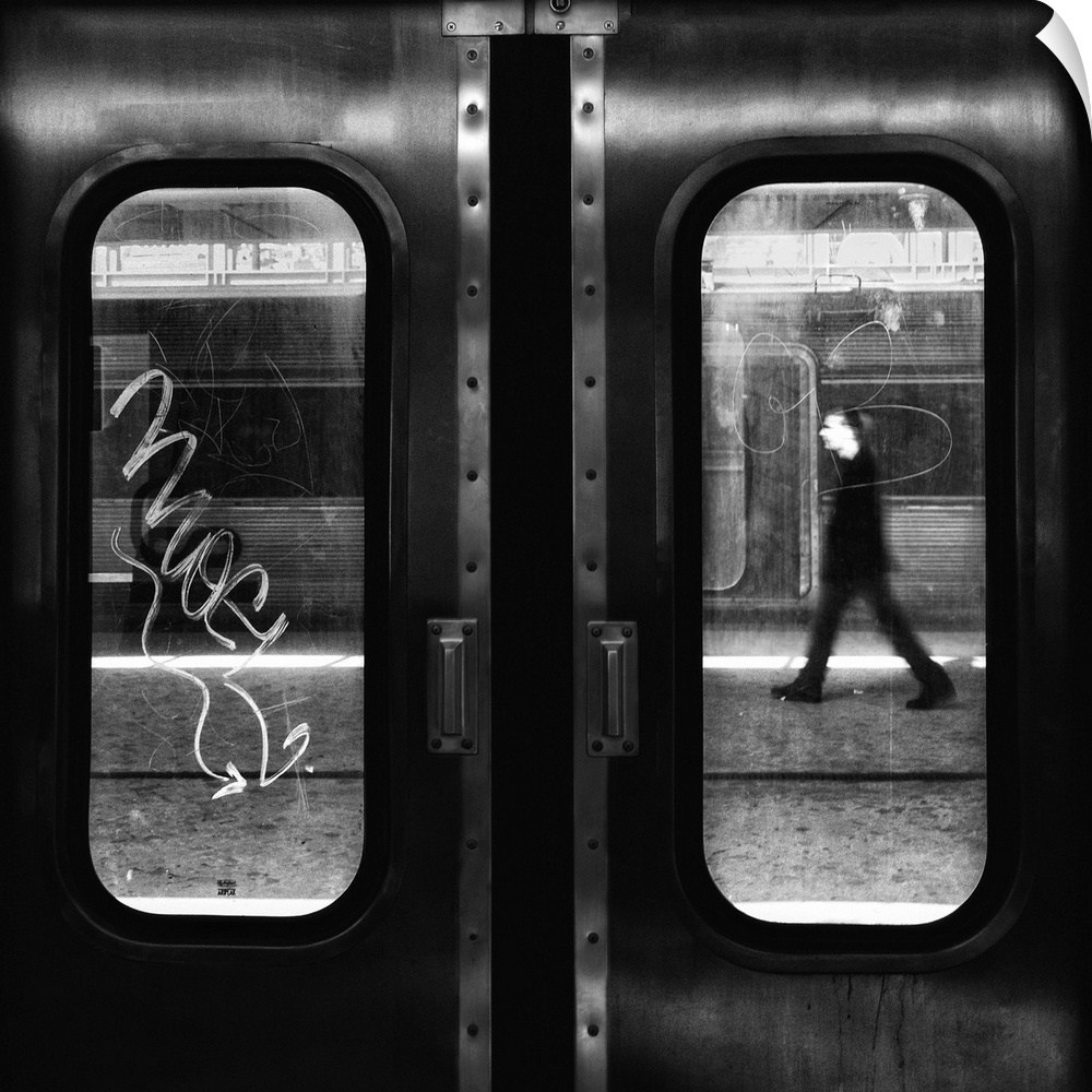 The doors and windows of a train car with graffiti on the glass and a man walking past.