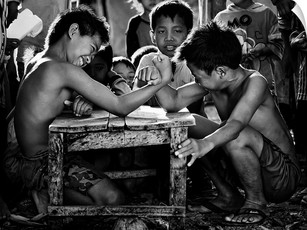 Children kneeling at a small table arm wrestling.